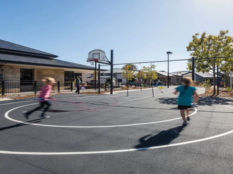 Eine Person reinigt leicht dunkle Gummifliesen auf einer Terrasse mit einem Gartenschlauch.